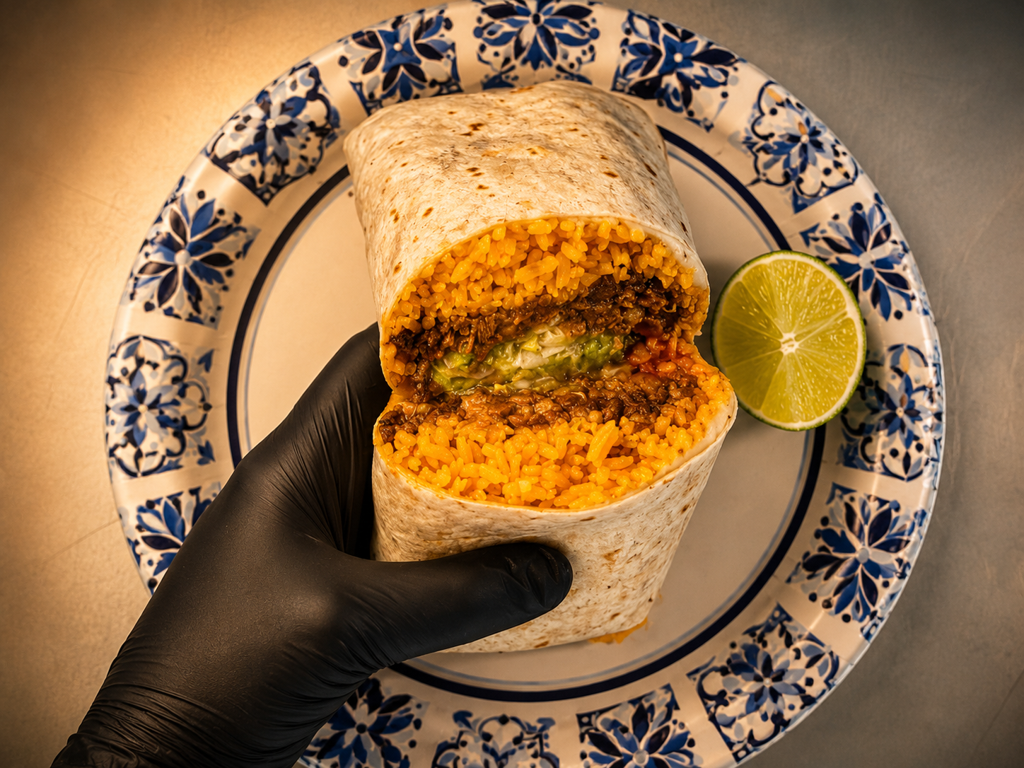 A burrito cut open to show rice, meat and guacamole, held in a gloved hand