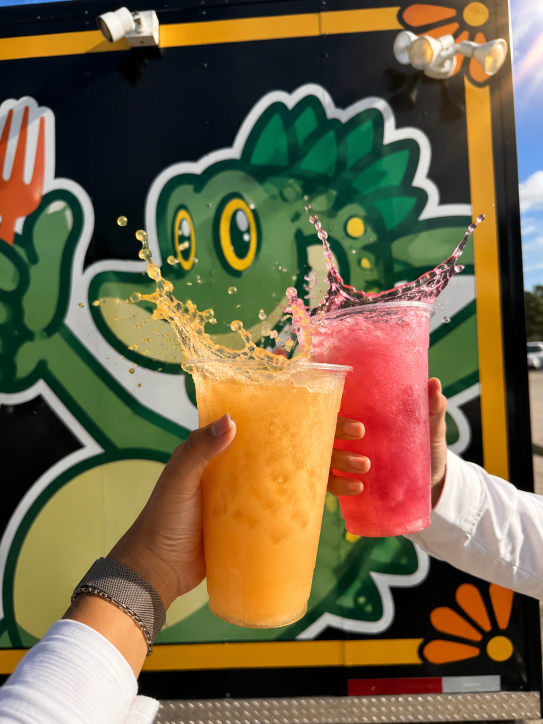 Two frozen drinks held up in front of the green mascot painted on our truck